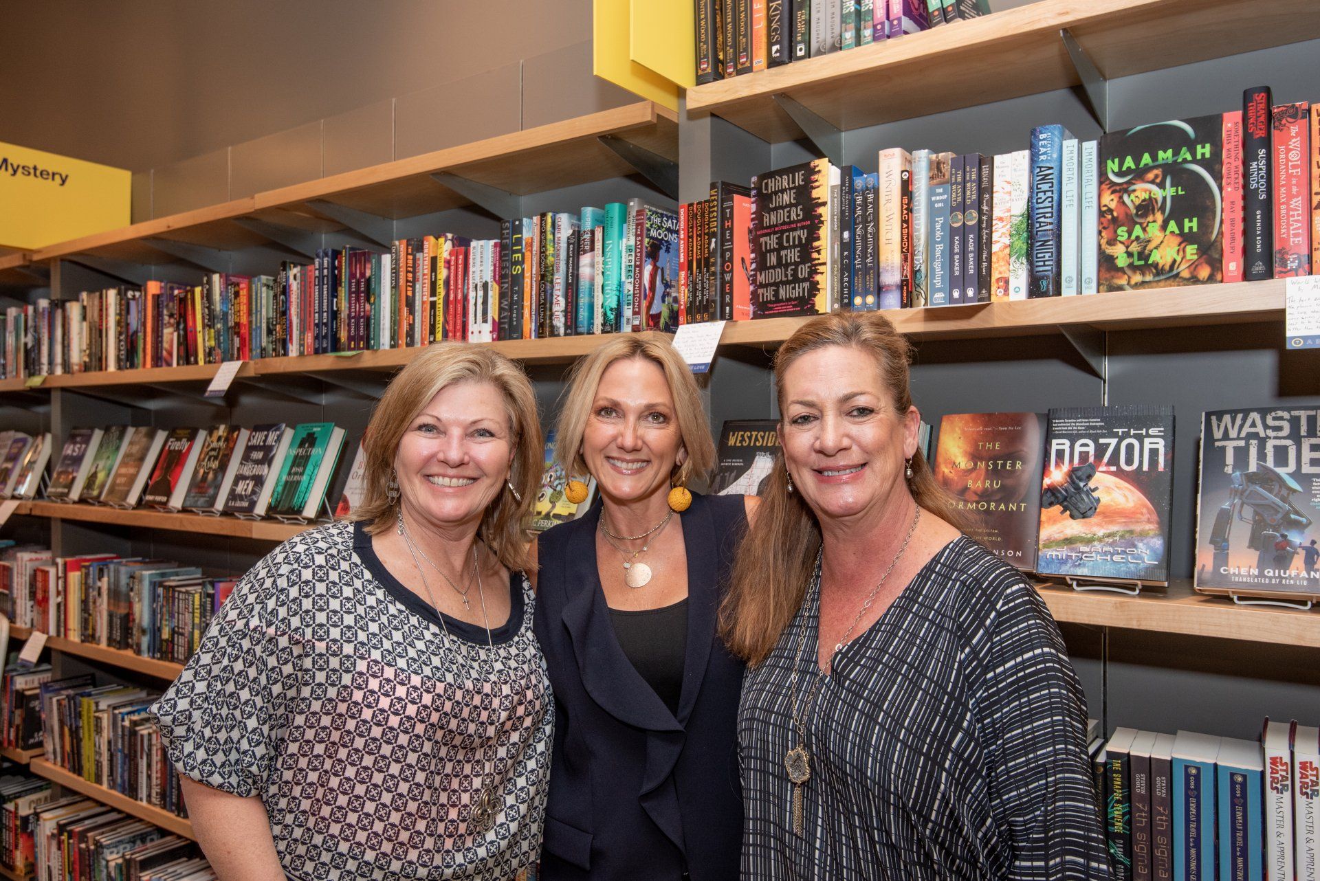 Three women are posing for a picture in front of a bookshelf in a library.