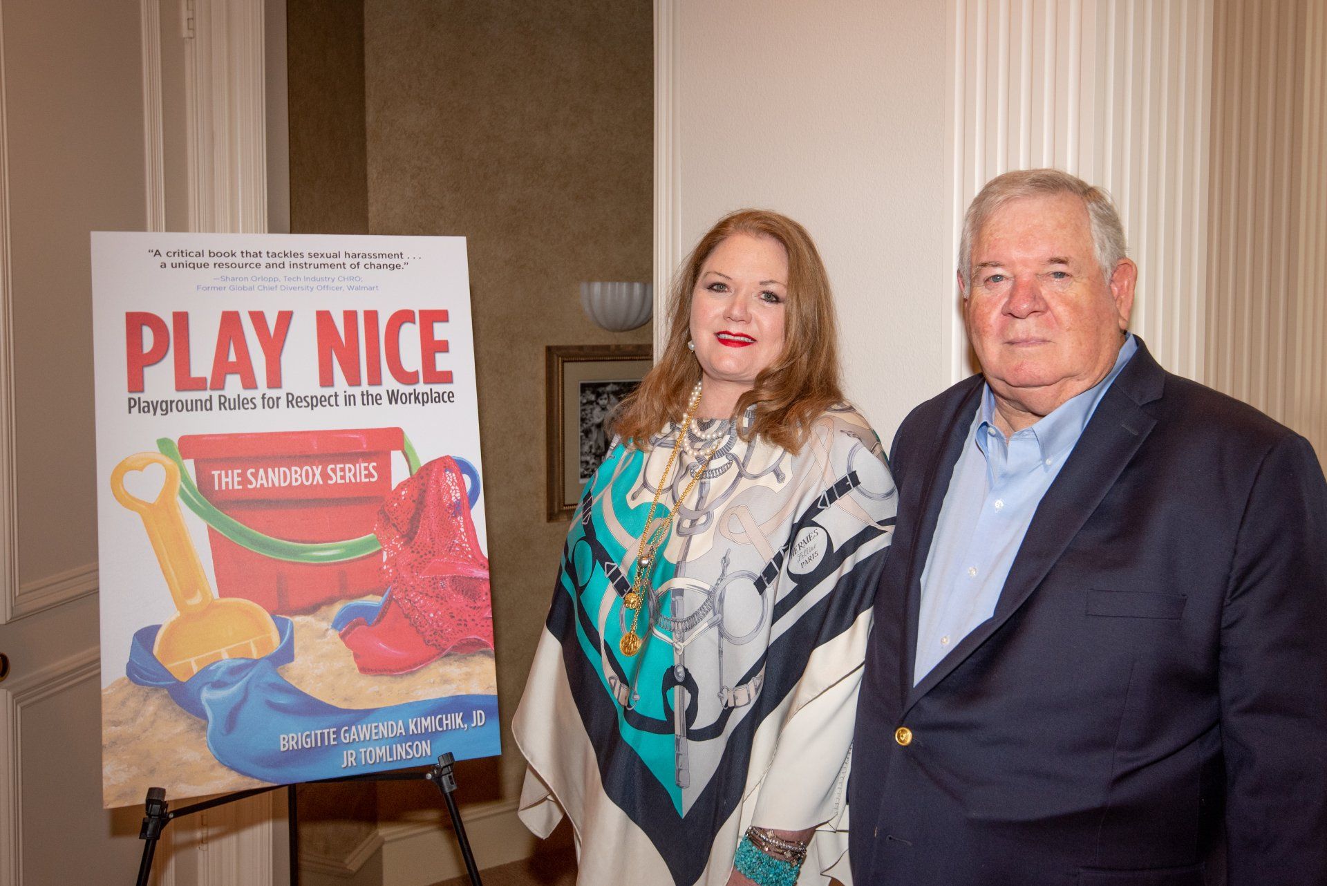 A man and a woman are standing next to each other in front of a play nice sign.