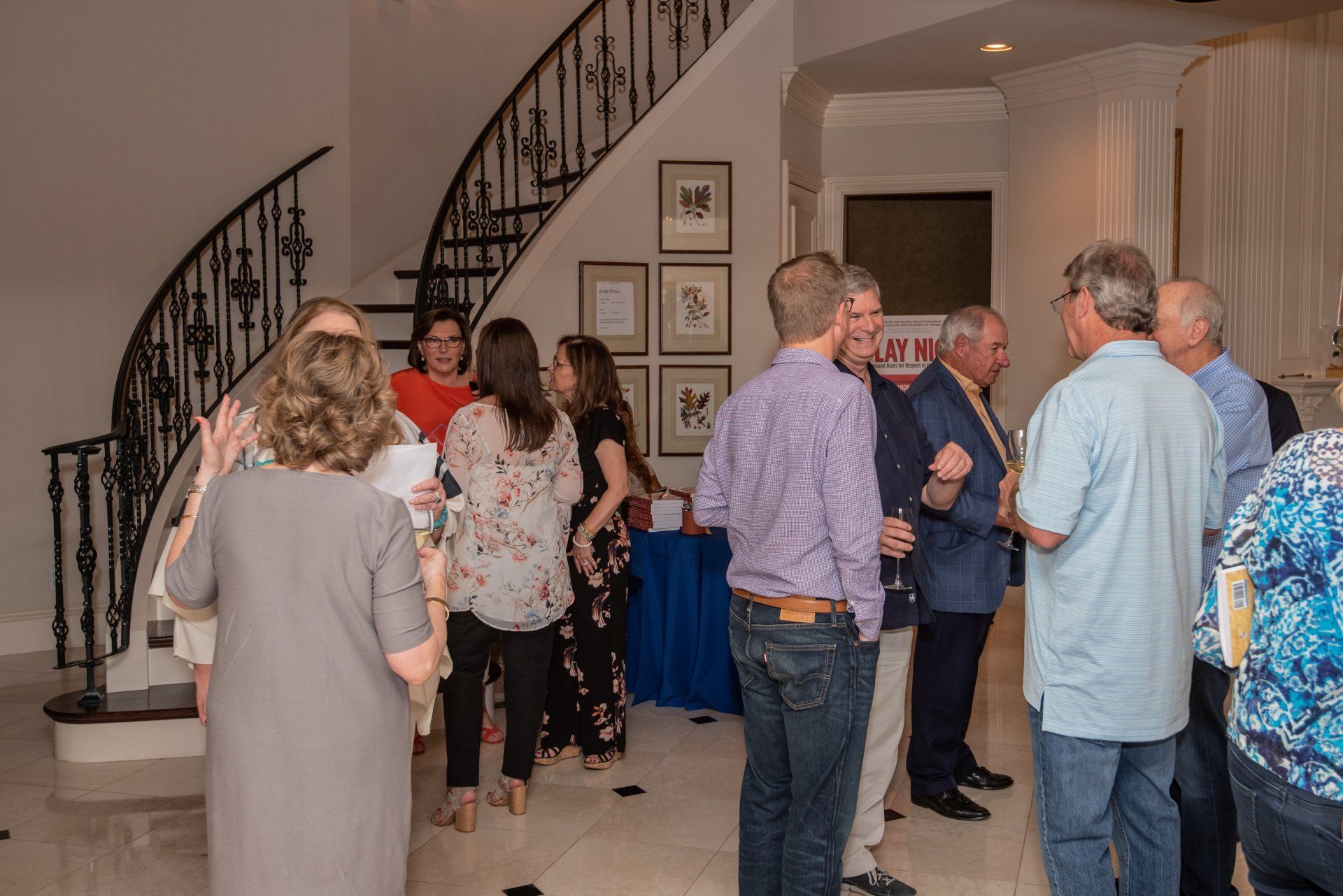 A group of people are standing in a room with a staircase in the background.