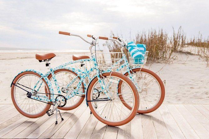 Two teal beach cruiser bicycles parked on a wooden boardwalk, near the beach.