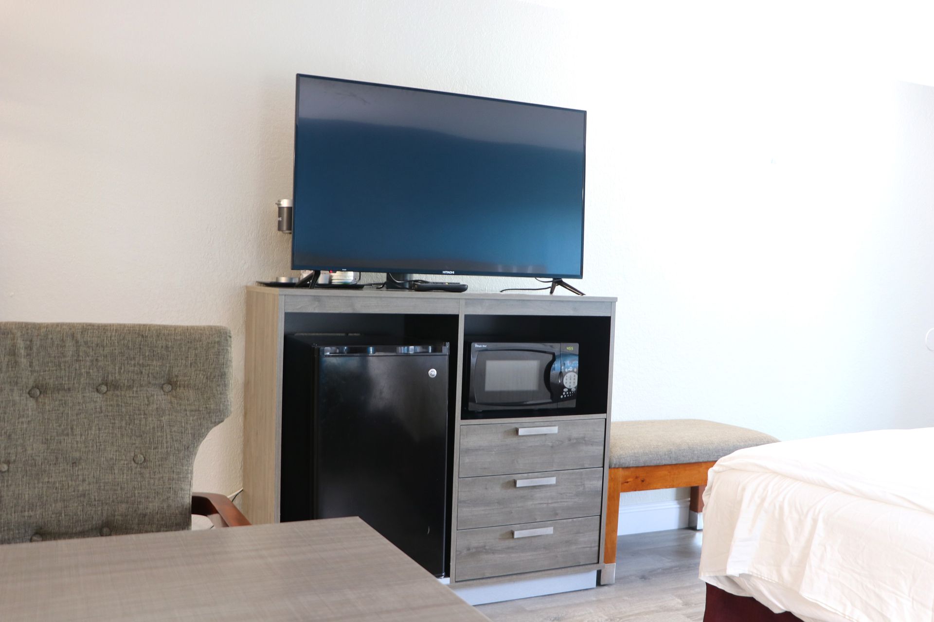 A hotel room with a TV, mini-fridge, microwave, and dresser. Includes a bed and table.