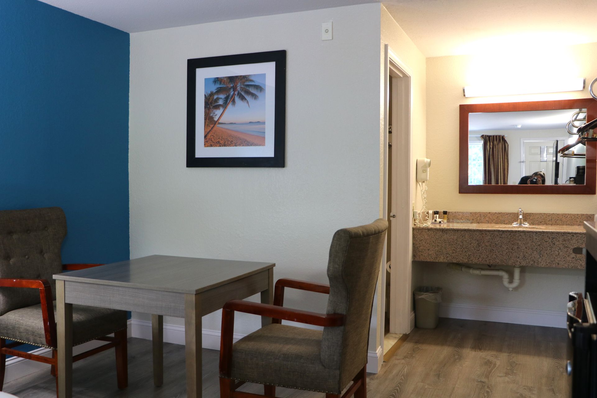 Hotel room with table, chairs, artwork, vanity, and open doorway to the bathroom.
