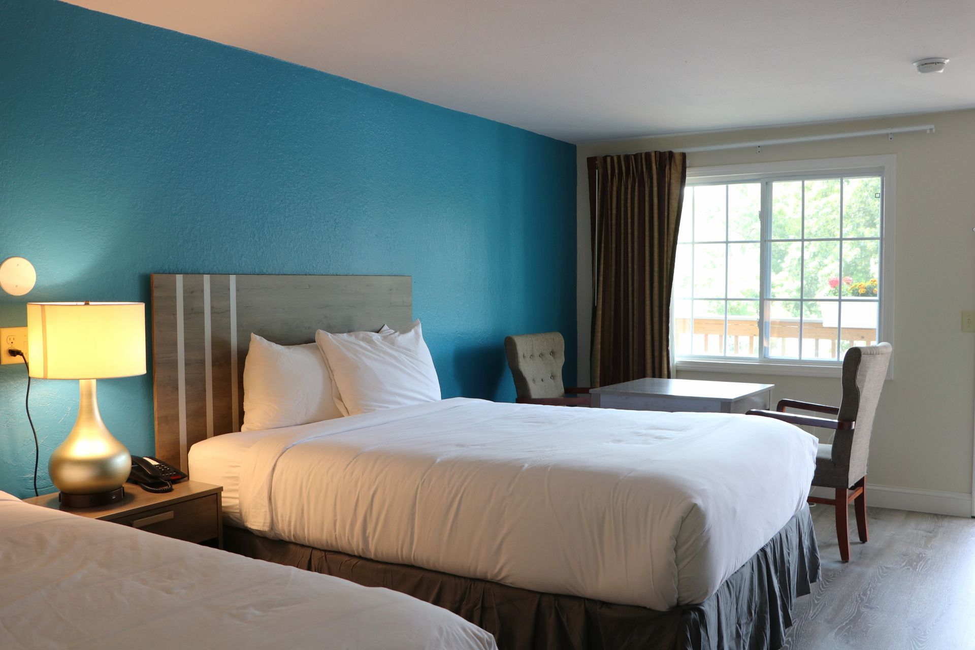 Two beds in a hotel room with a blue accent wall and a window.