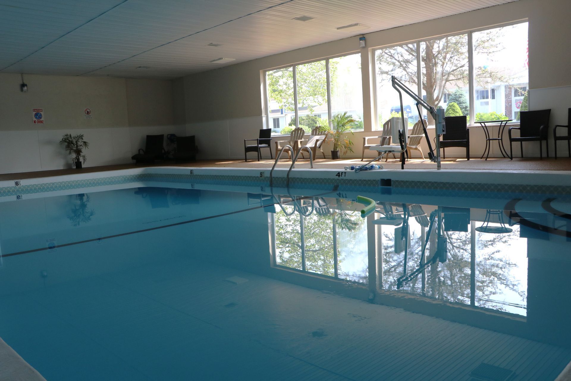Indoor swimming pool with clear water, windows, and chairs.