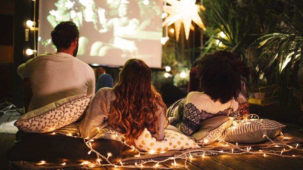 People watching a movie outdoors at night, sitting on pillows. Fairy lights and a star-shaped decoration visible.