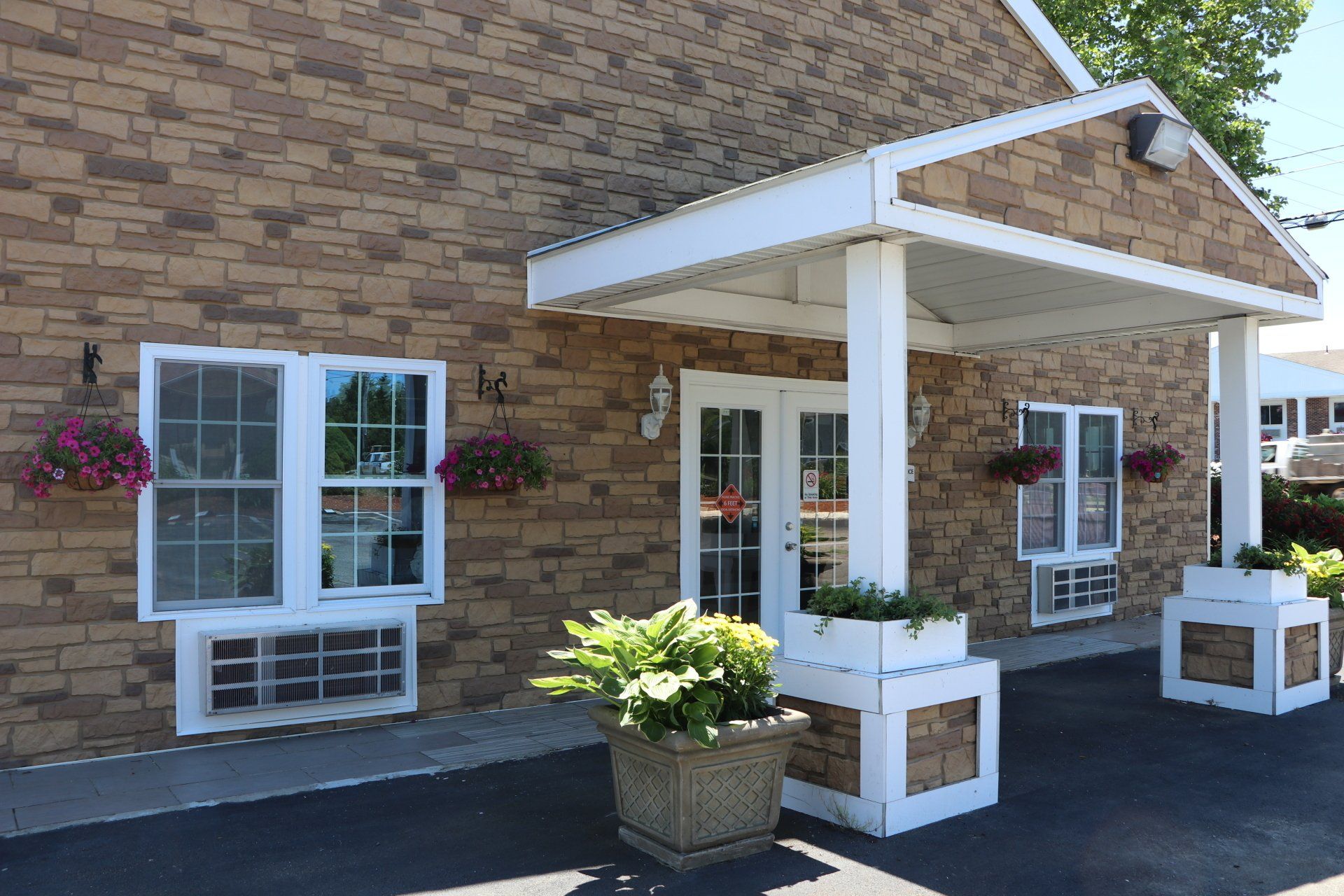 Exterior of a building with stone-like facade, entrance under a white awning, windows with flower boxes.