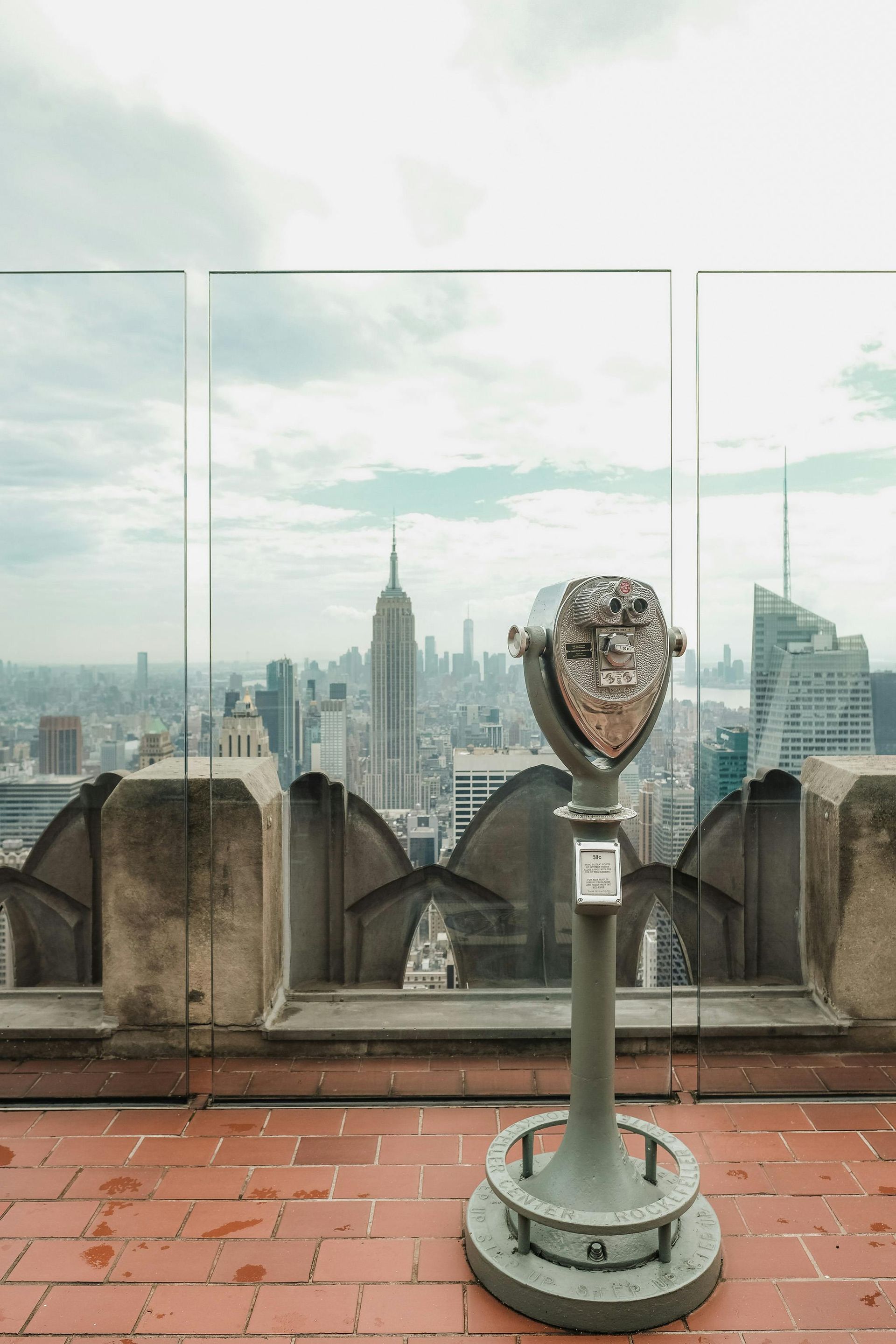 A telescope is sitting on top of a brick patio overlooking a city skyline.