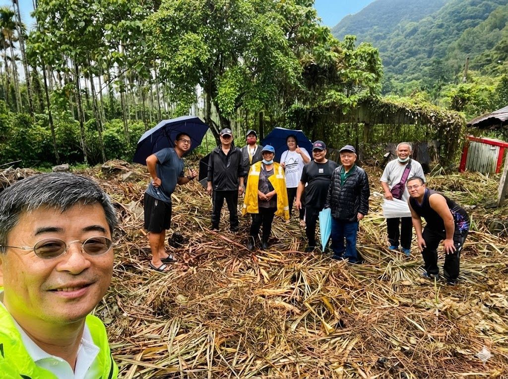 一群人在戶外建築附近擺姿勢拍照,背景是山。許多人面帶微笑。
