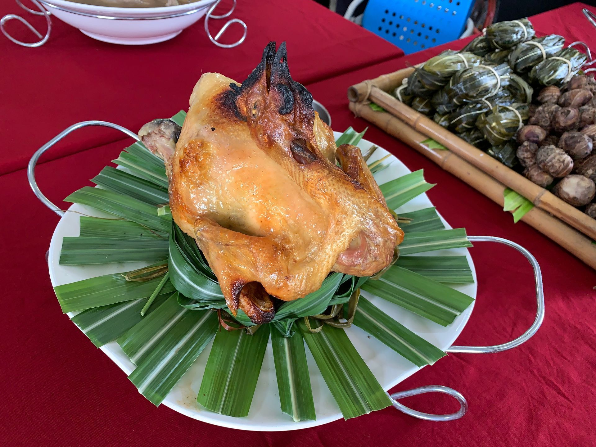 中興紅羽1982土雞烤雞放在鋪著綠葉的盤子裡，旁邊是其他菜餚，擺放在鋪著紅色桌布的桌子上。