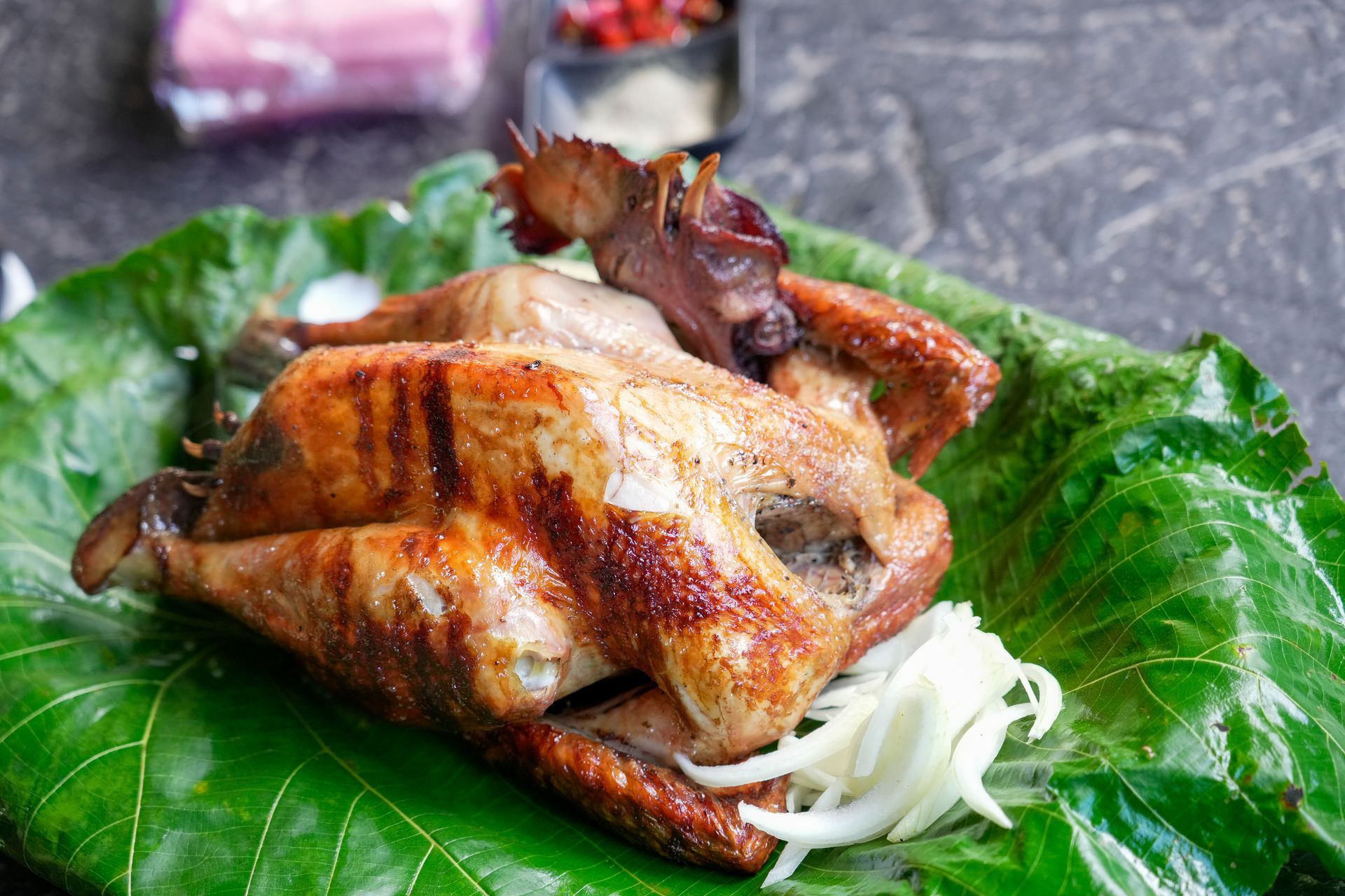 中興紅羽1982土雞烤雞放在一片大綠葉上，配上一小碟醬汁和一份洋蔥。