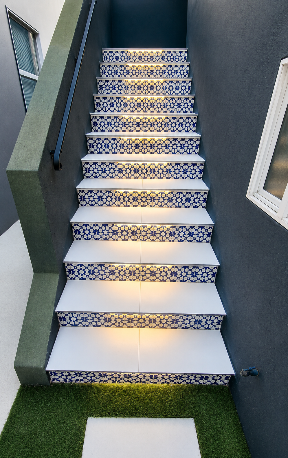 Outdoor staircase with patterned tile steps, gray walls, and a small grass landing at the bottom Outdoor staircase with patterned tile steps, gray walls, and a small grass landing at the bottom