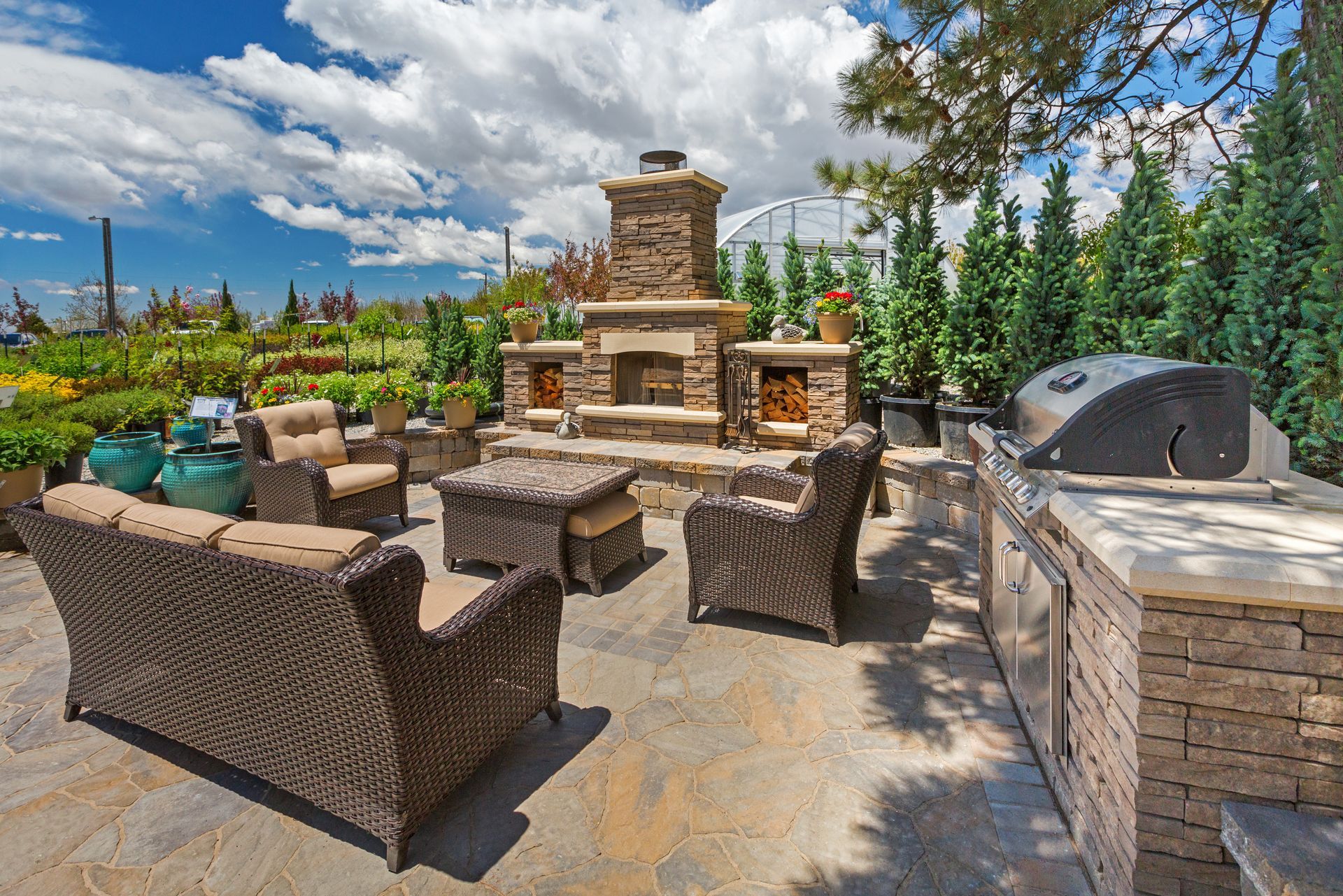 Outdoor stone patio with wicker seating and a built-in fireplace under a partly cloudy sky Outdoor stone patio with wicker seating and a built-in fireplace under a partly cloudy sky