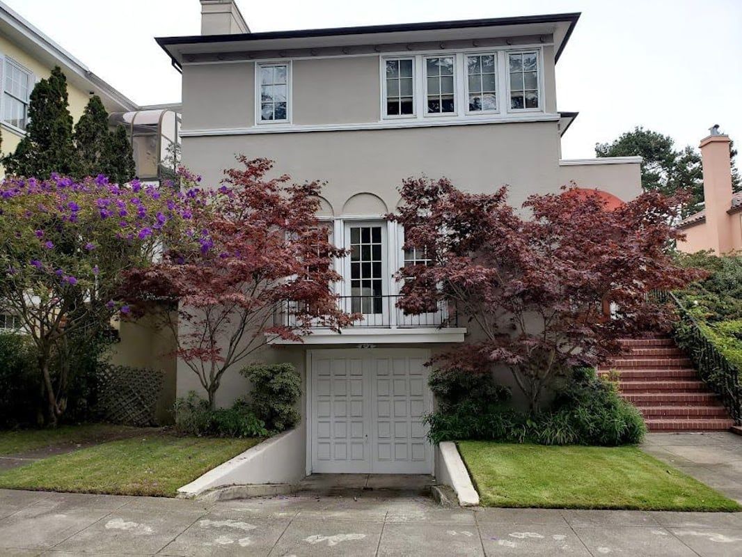Two-story white house with red-leafed trees, a garage, and steps leading to the front entrance.