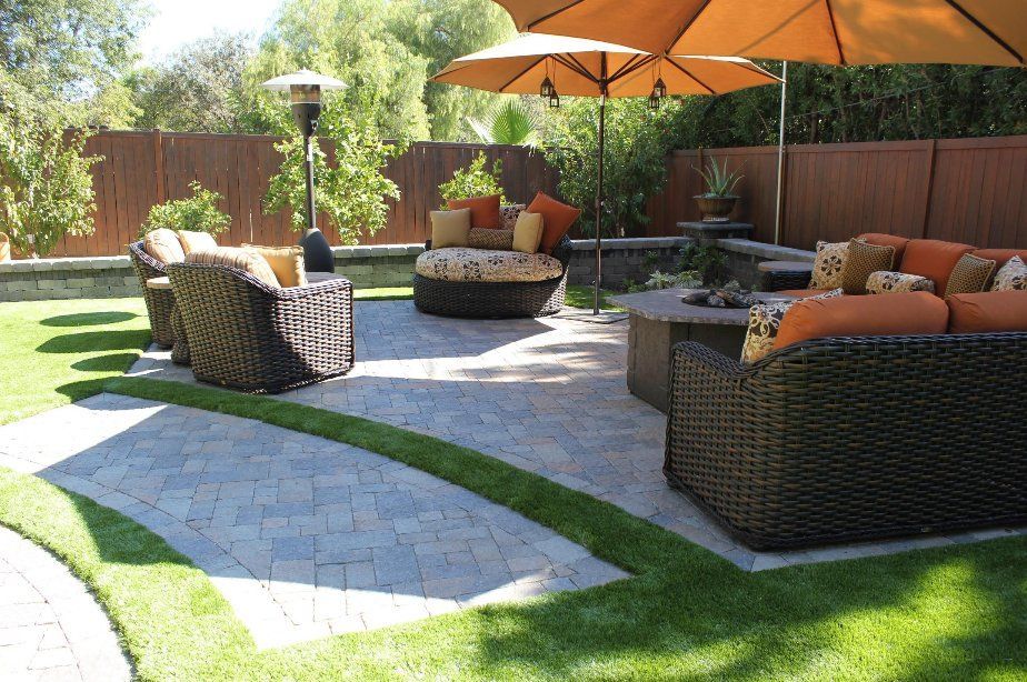 Sunny backyard patio with wicker seating, orange umbrellas, and curved stone paths on green lawn Sunny backyard patio with wicker seating, orange umbrellas, and curved stone paths on green lawn