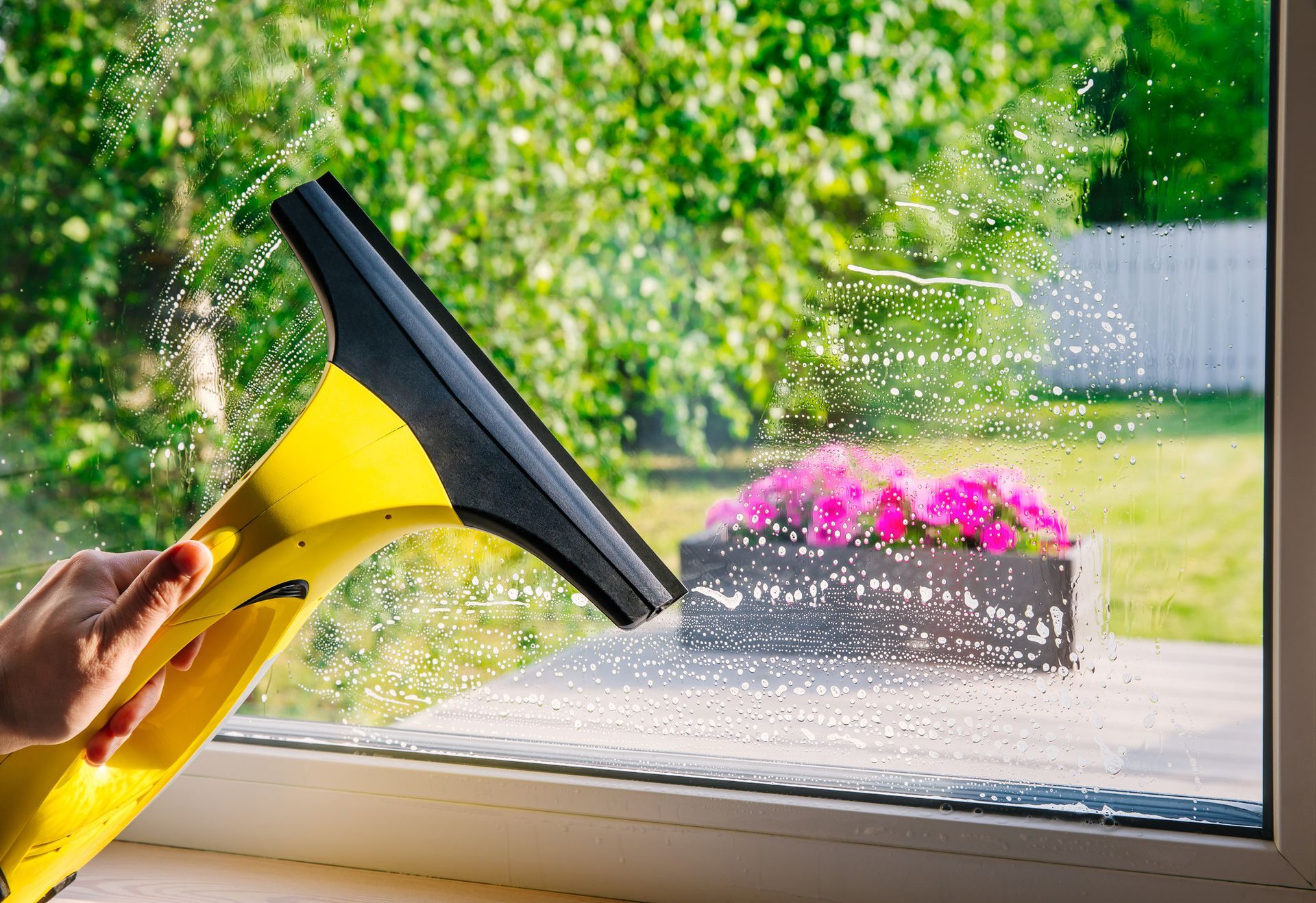 A person is cleaning a window with a yellow window cleaner.
