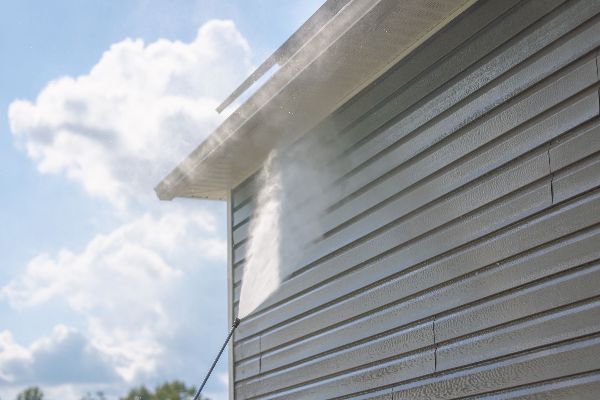 A man in a yellow jacket is cleaning a house with a high pressure washer.