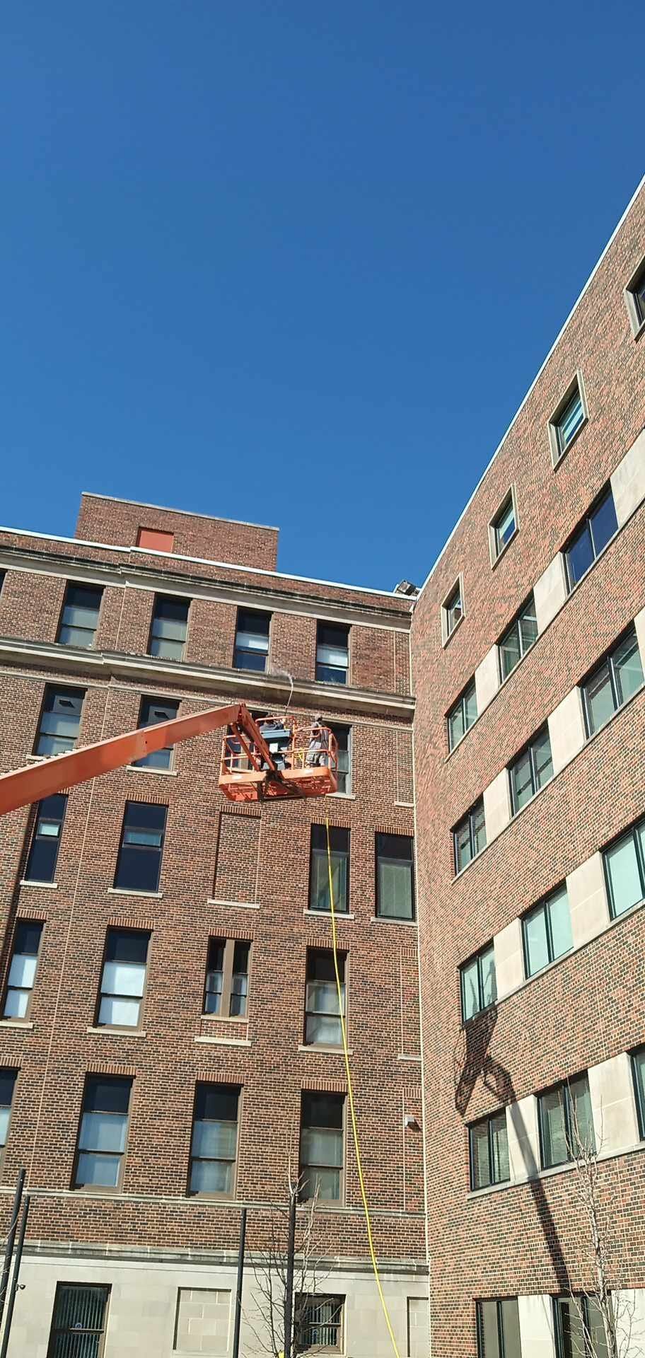 A man in a yellow jacket is using a high pressure washer to clean a sidewalk.