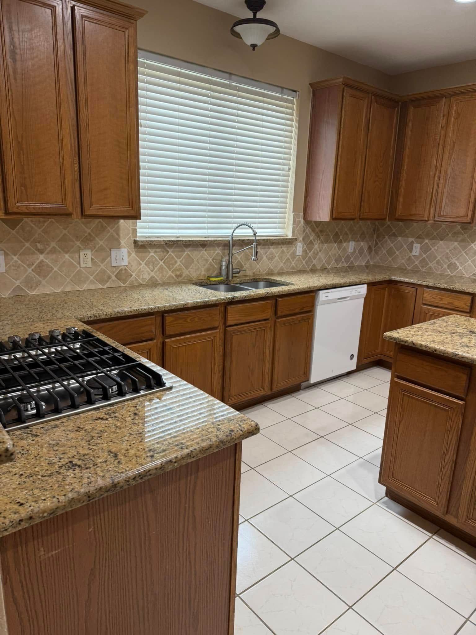 A kitchen with wooden cabinets , granite counter tops , a stove and a sink.
