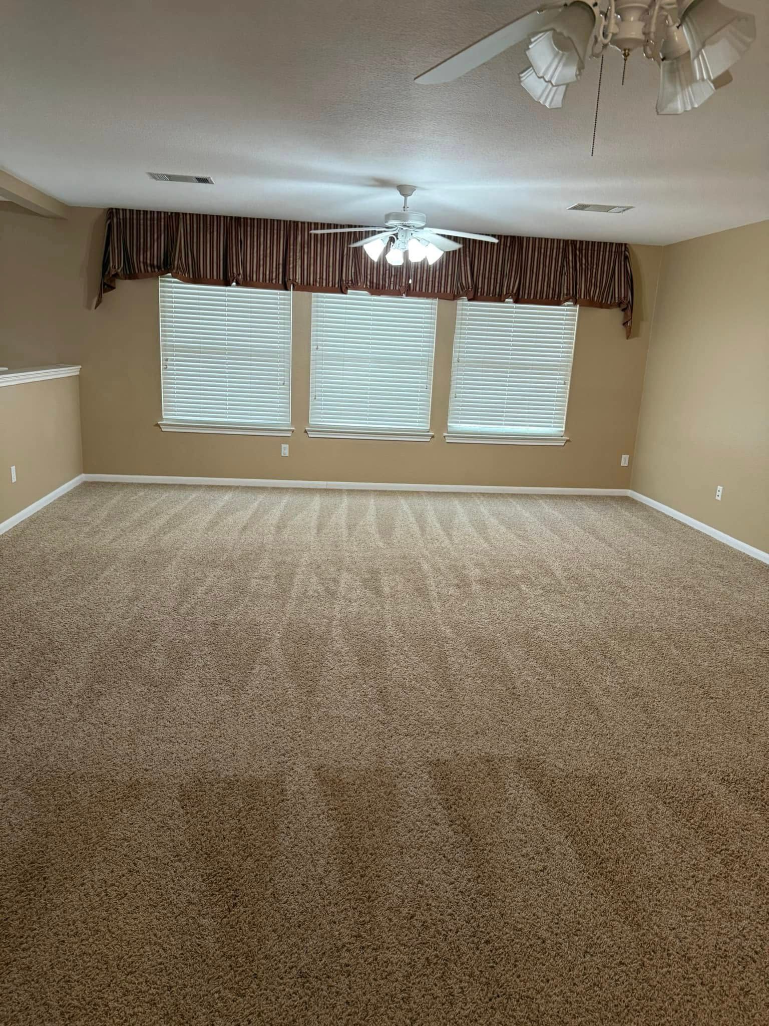 An empty living room with a ceiling fan and a lot of windows.
