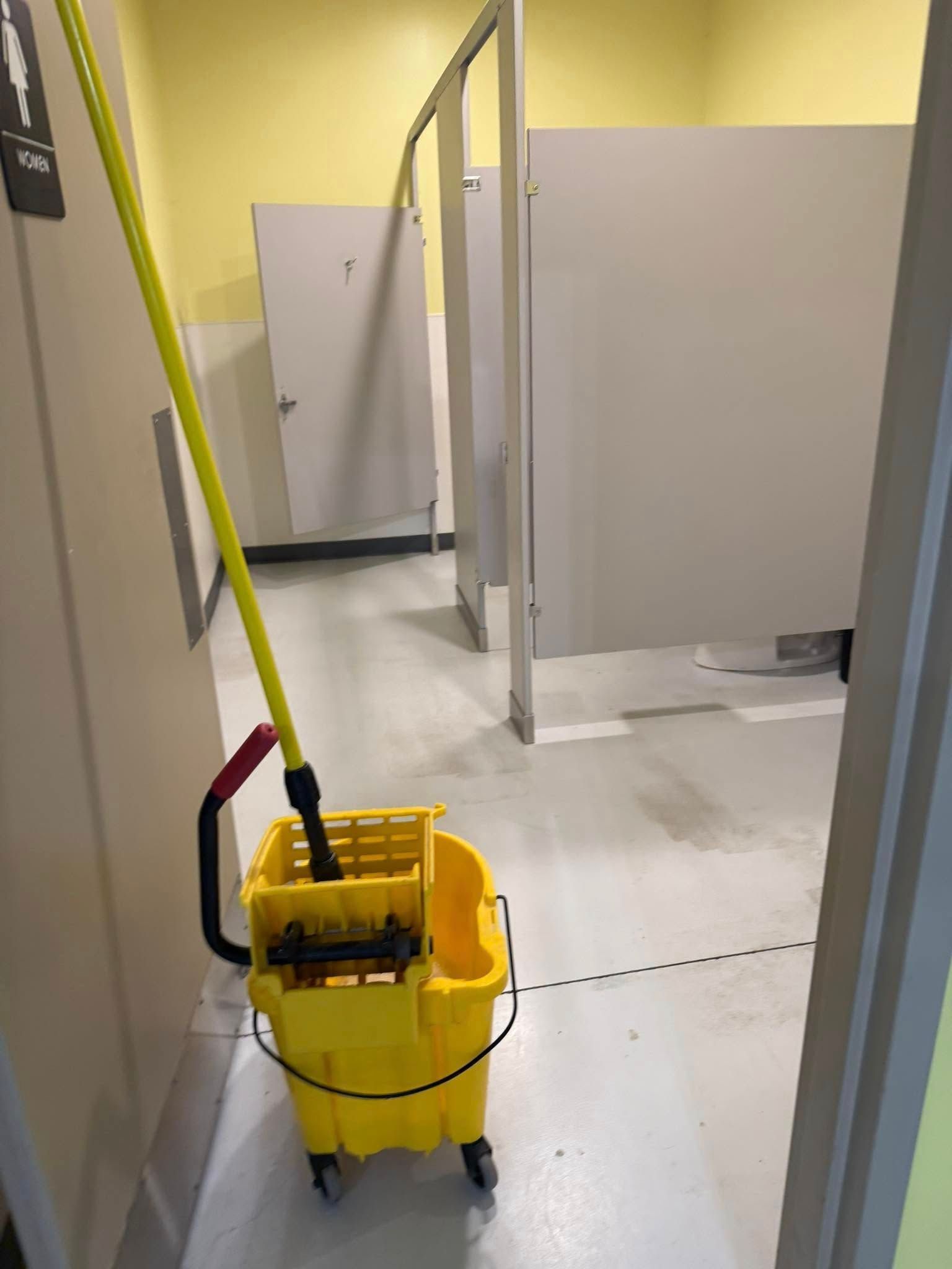 A yellow mop bucket is sitting in a bathroom next to a toilet.