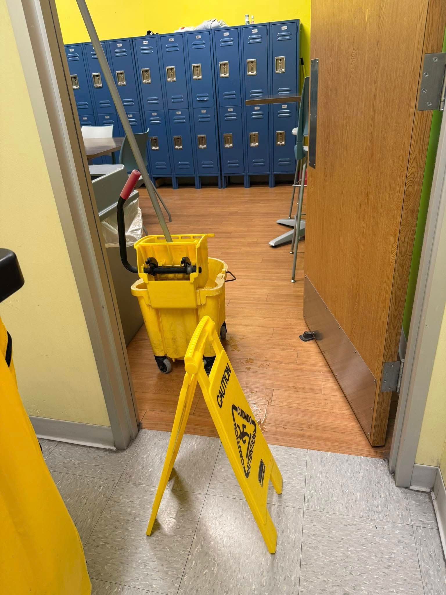 A yellow wet floor sign is sitting on the floor next to a mop bucket.