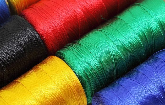 There are many different colored spools of thread stacked on top of each other.
