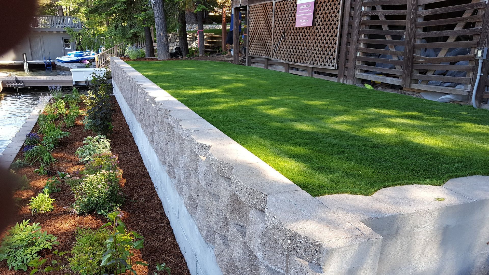 A concrete wall surrounds a lush green lawn next to a body of water.