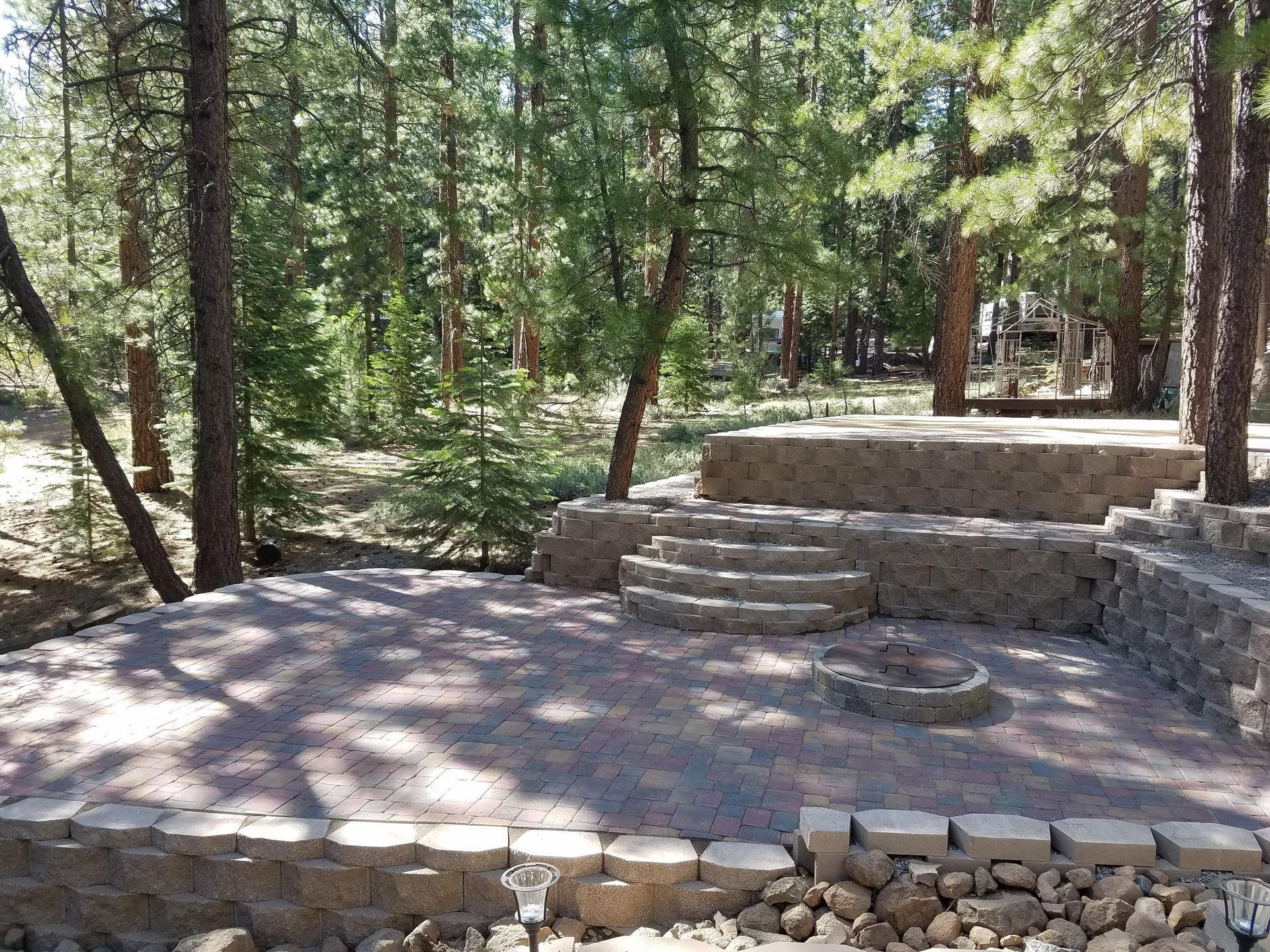 A stone patio with stairs and a fire pit in the middle of a forest.