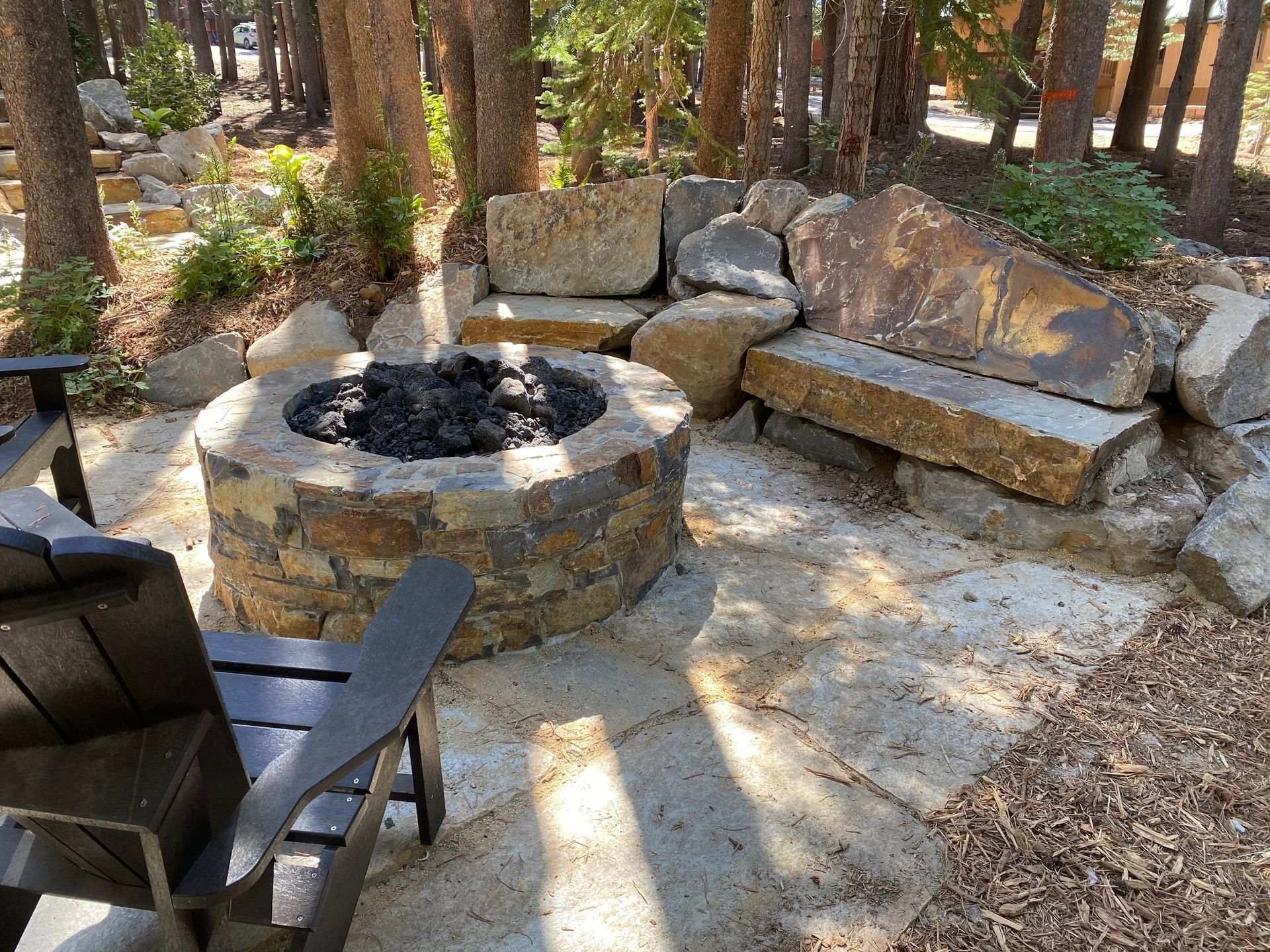 A fire pit surrounded by rocks and chairs in the middle of a forest.