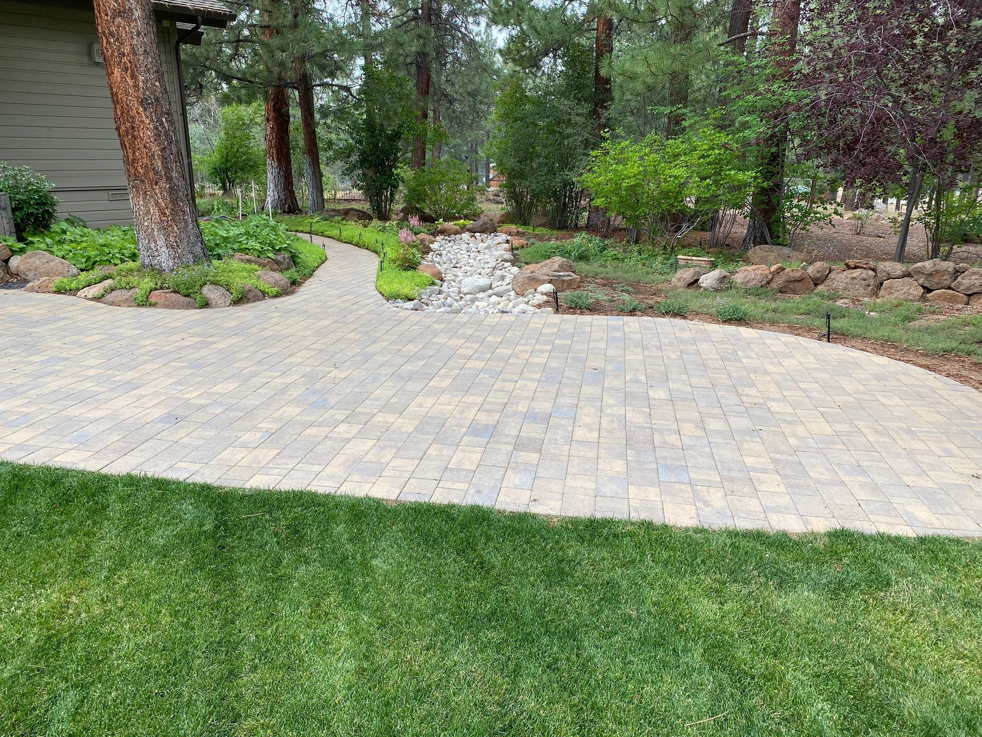 A brick walkway leading to a house surrounded by trees and grass.