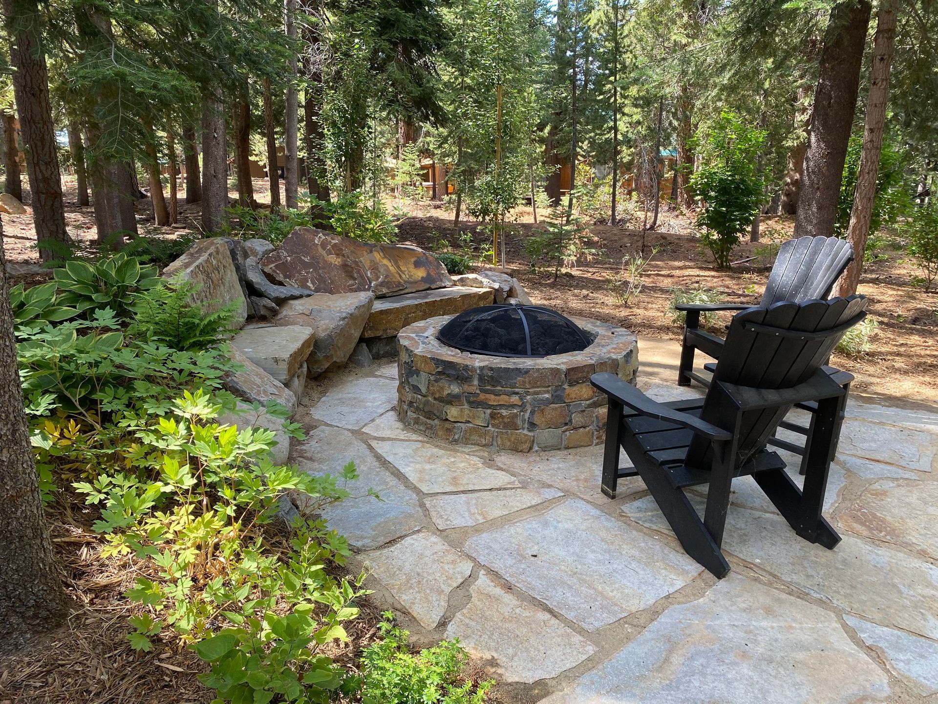 Two chairs are sitting next to a fire pit in the middle of a forest.