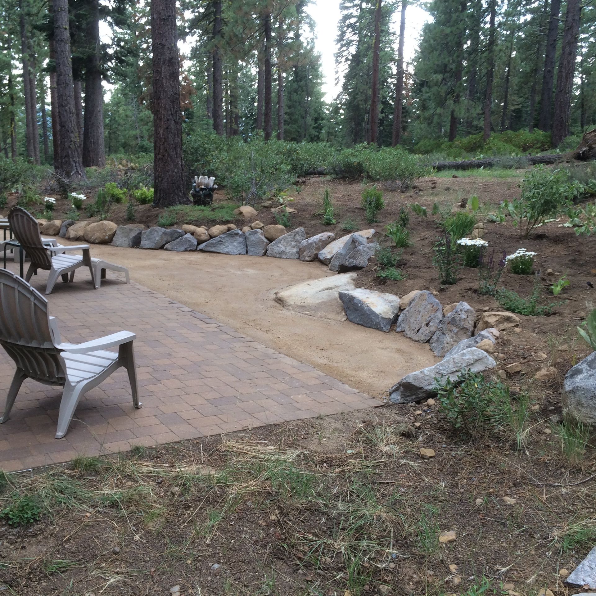 A patio in the middle of a forest with chairs and rocks