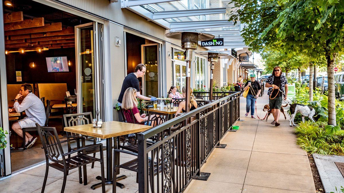 A group of people are sitting at tables outside of a restaurant.