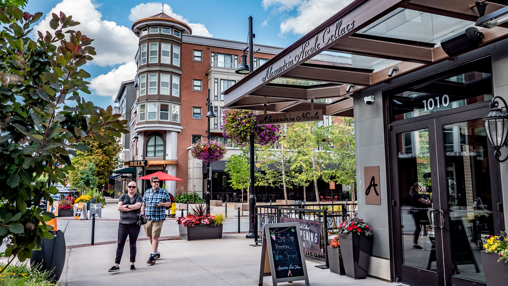 A couple of people are walking down a sidewalk in front of a building.