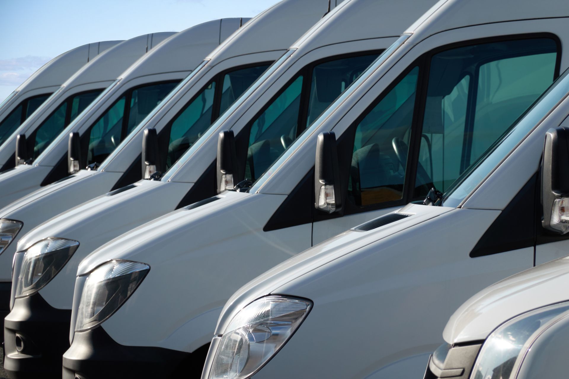 A row of white vans are parked in a parking lot.