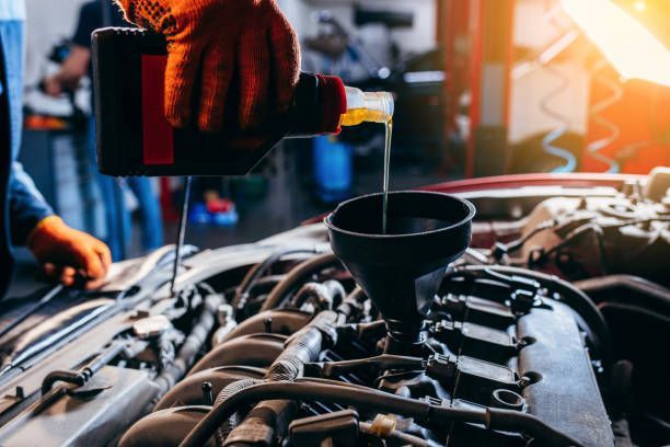 A mechanic is pouring oil into a funnel on a car engine.