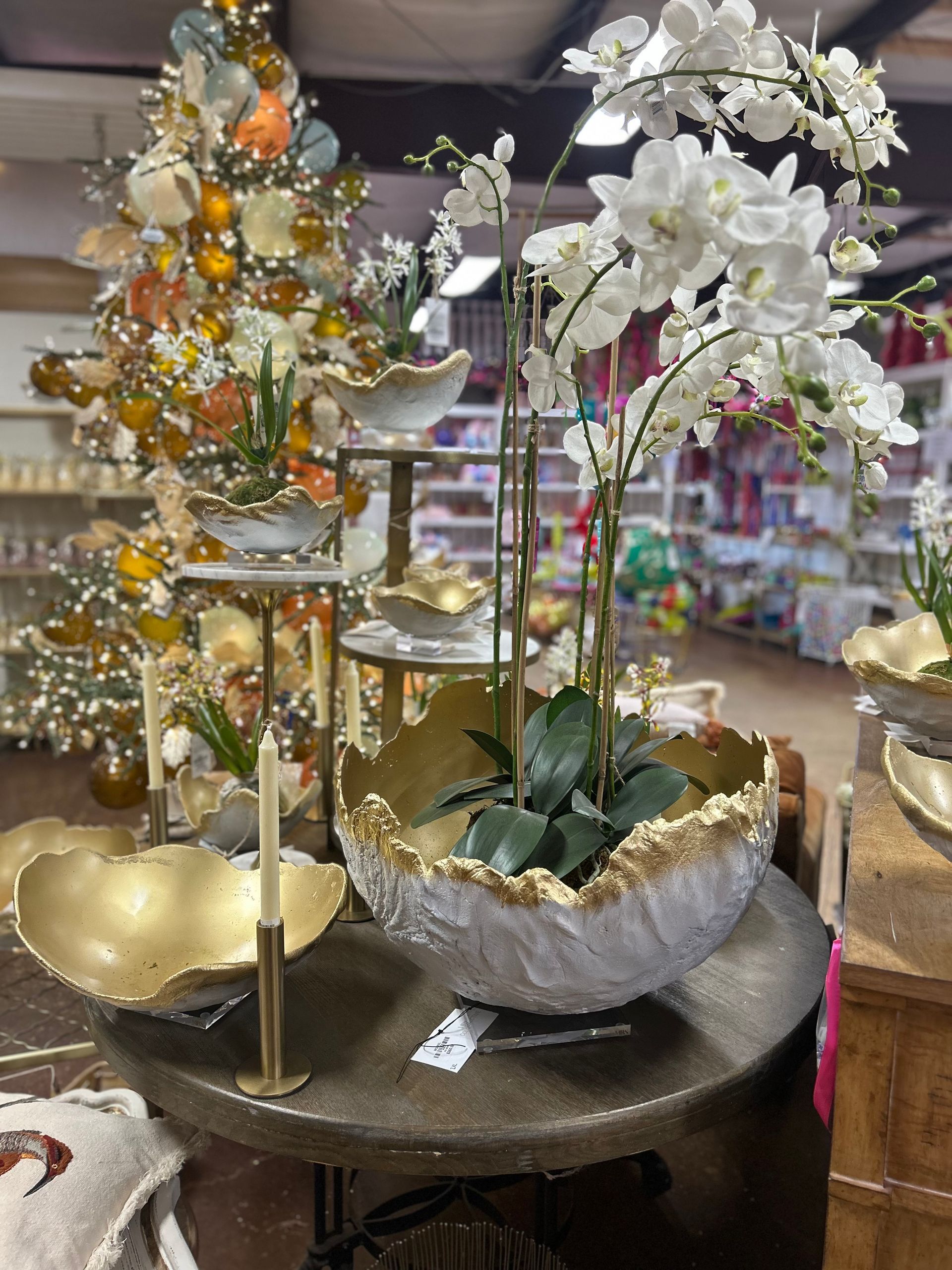 A table with a vase of flowers on it and a christmas tree in the background.