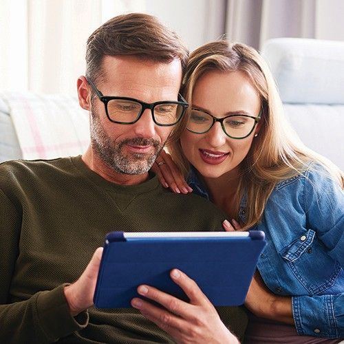 A man and a woman are sitting on a couch looking at a tablet.