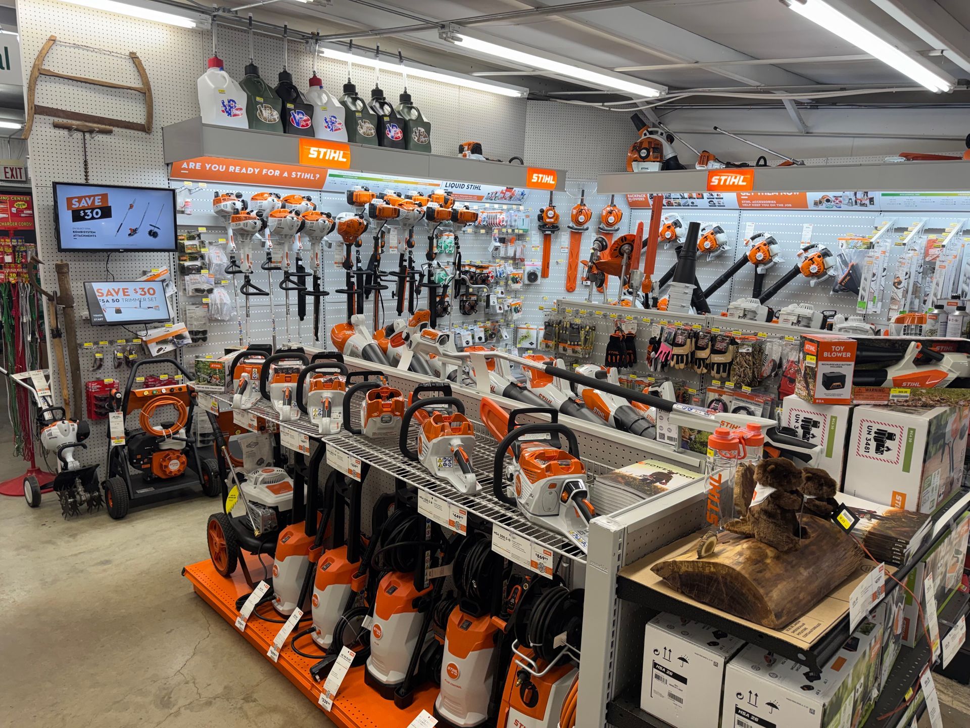 Person trimming a bush with a teal hedge trimmer, wearing gloves and a plaid shirt.