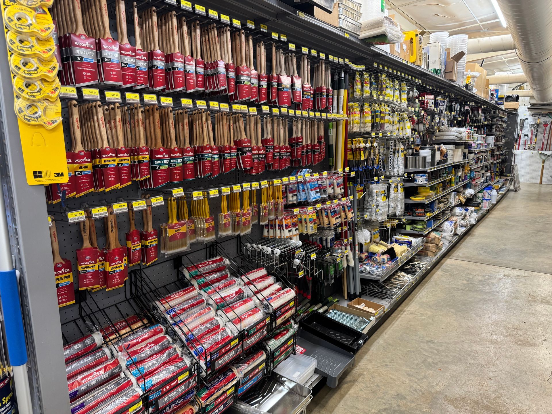 Paint brushes and tools on display at a hardware store, various colors, in a long aisle.