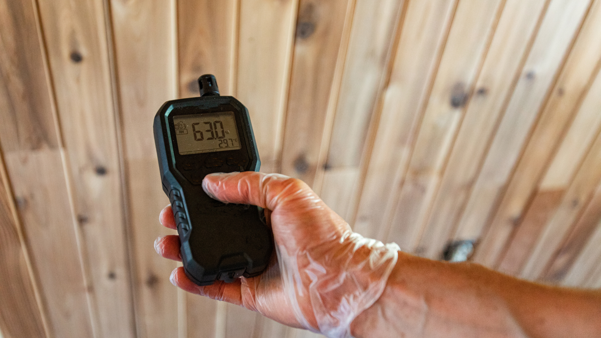 A person is holding a digital thermometer in their hand in front of a wooden wall.