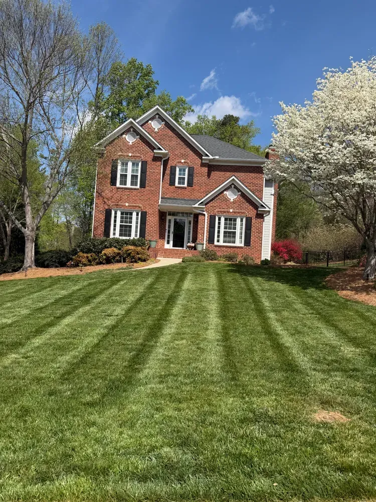 Brick two-story house with a manicured green lawn, blue sky, and blooming trees in spring
