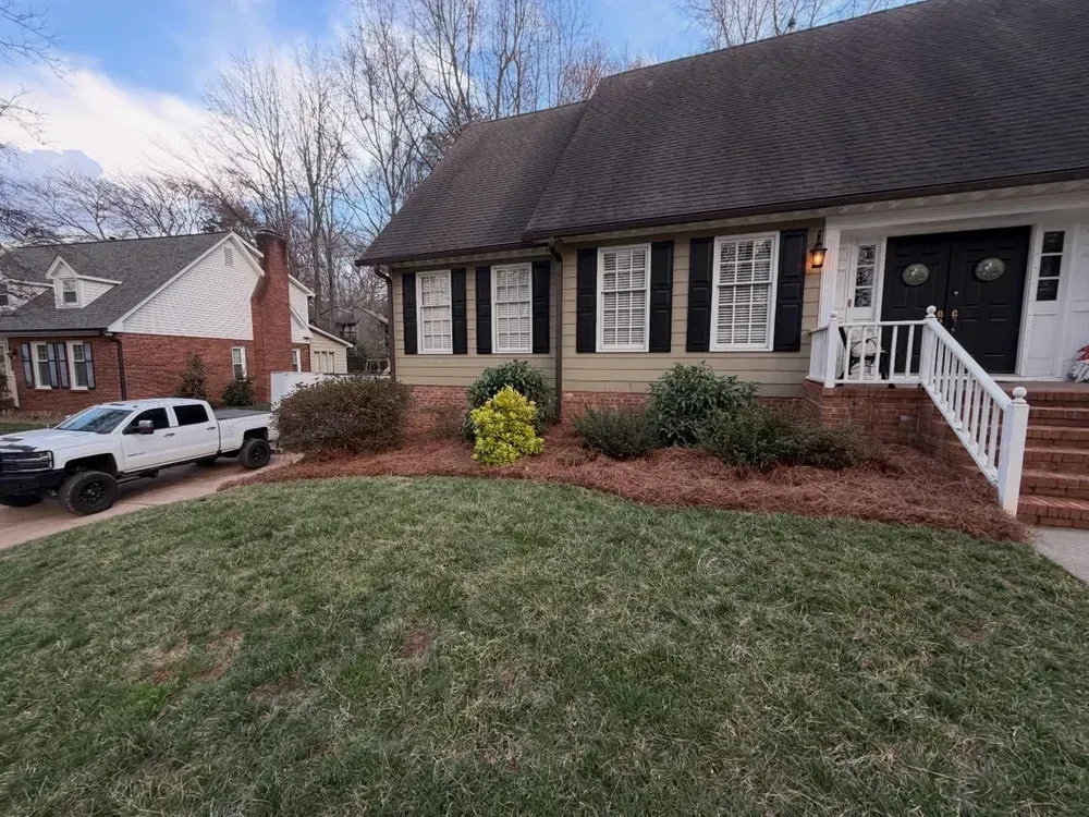 Single-story brick house with dark roof, white trim, front porch, and landscaped yard on a cloudy day