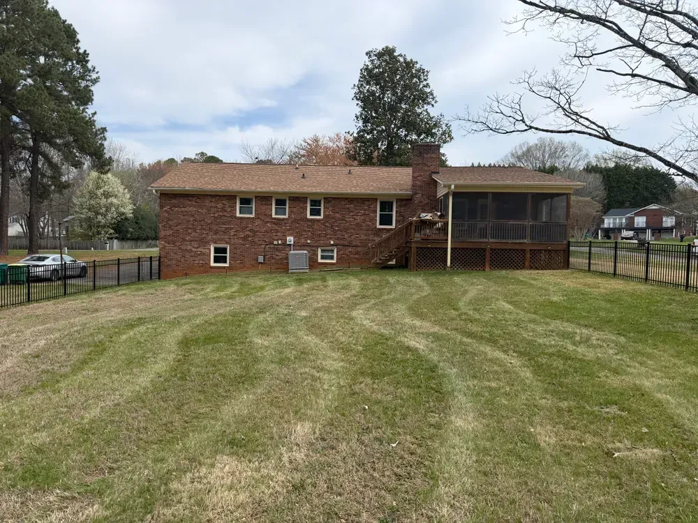 Brick house with screened porch and wide mowed backyard, viewed from the lawn