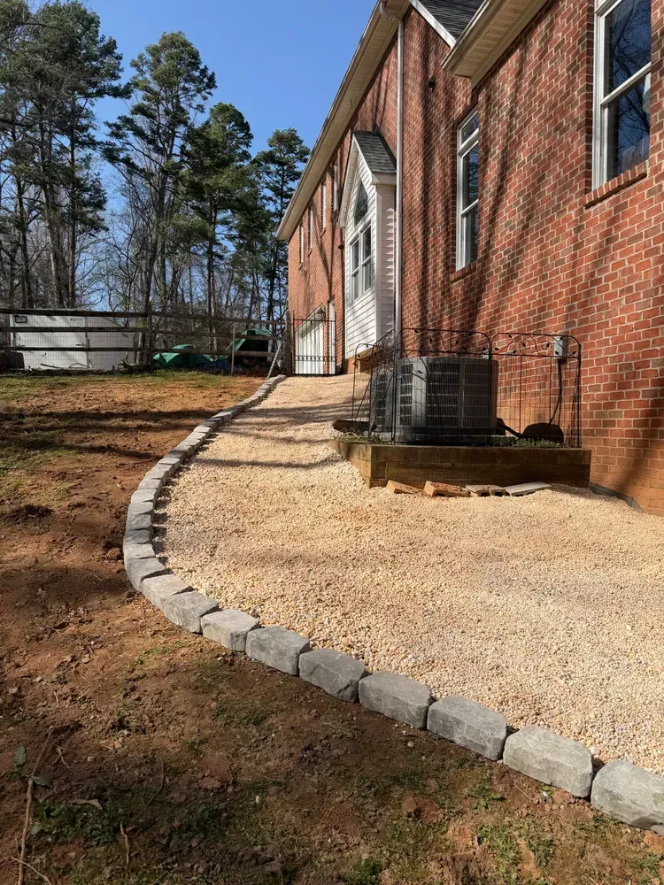 Brick house with a curved gravel walkway, stone edging, and an outdoor air conditioner unit