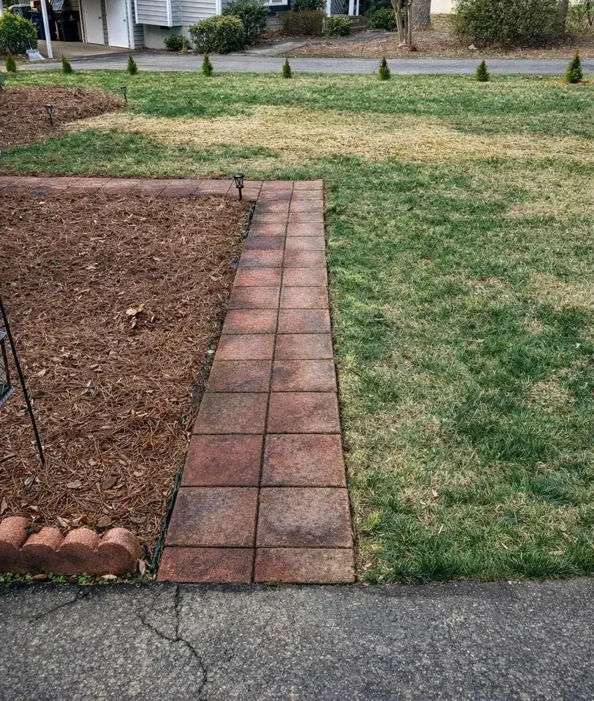 Brick walkway beside mulch bed and grassy lawn in a residential yard.