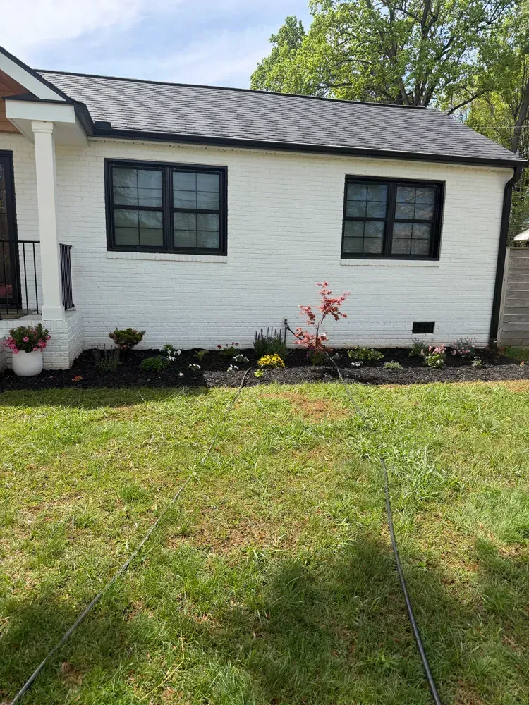 White brick house exterior with black-trimmed windows and a small flower bed in front