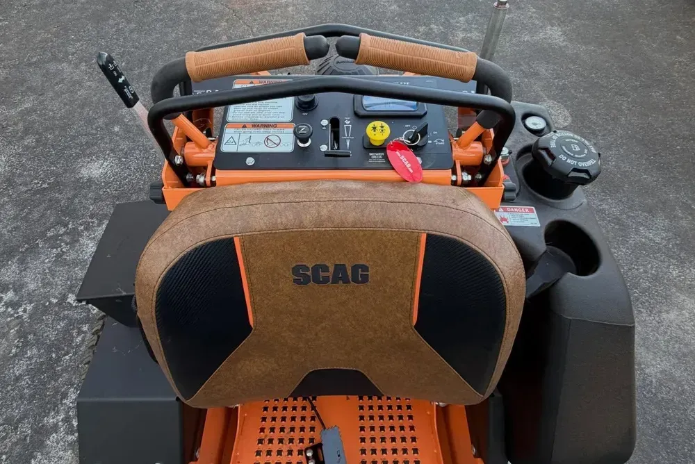 Top view of an orange SCAG lawn mower with control panel and steering handles on pavement