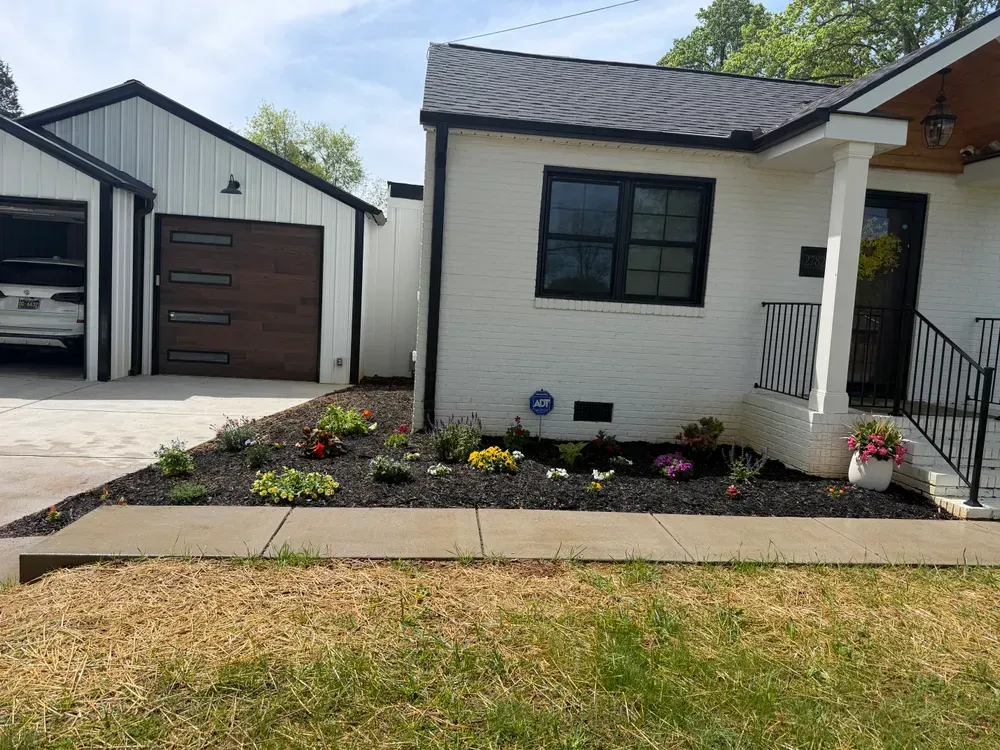 Modern white house with black trim, garage, front porch, and landscaped flower bed in front yard