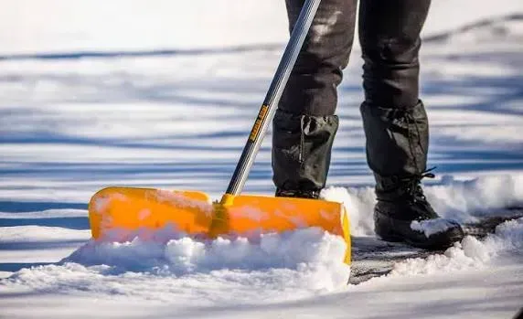 Person shoveling snow with an orange snow pusher on a snowy surface